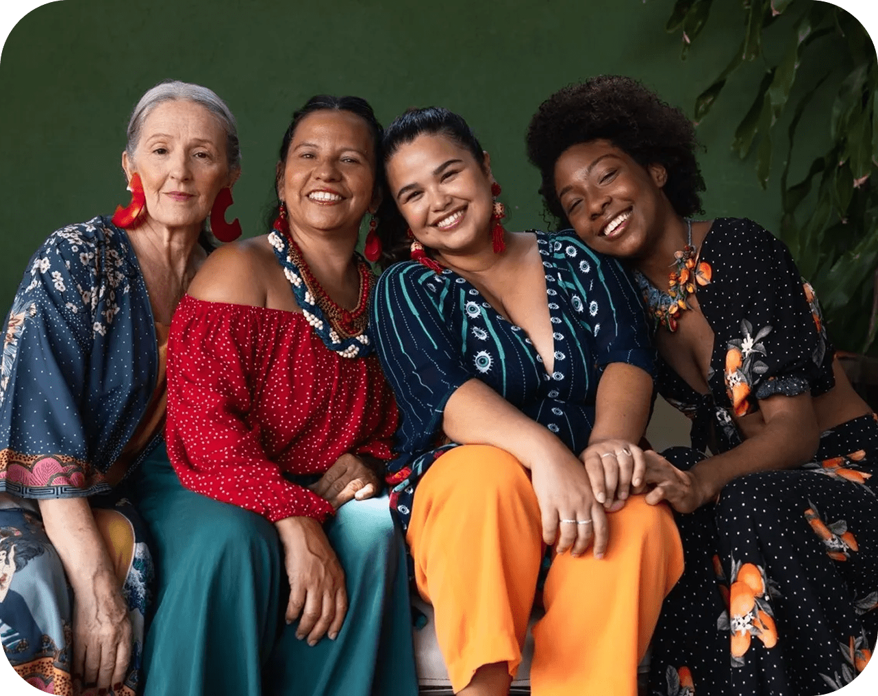 Four women smiling in colorful outfits.