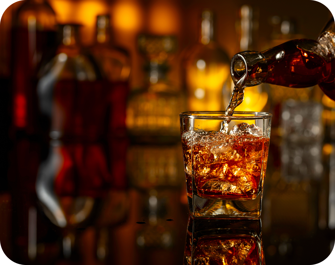 Pouring whiskey into glass with ice cubes.